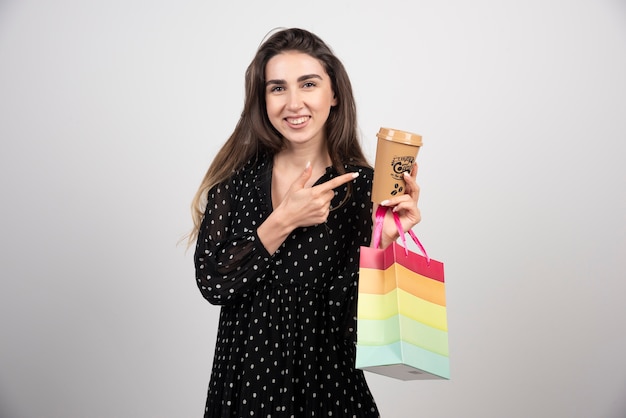 Modèle de jeune femme pointant sur une tasse de café et tenant un sac de magasin