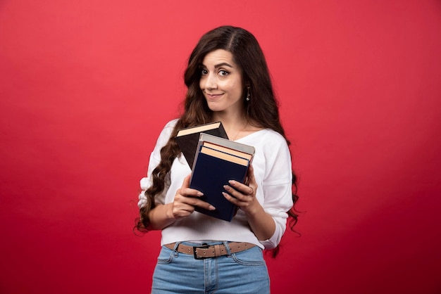 Modèle de jeune femme posant avec des livres sur fond rouge. photo de haute qualité
