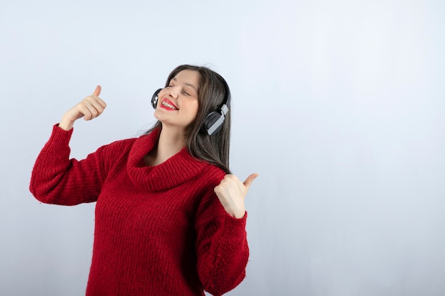 Modèle de jeune femme en pull rouge avec un casque montrant les pouces vers le haut