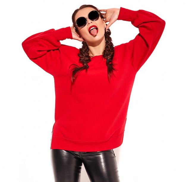 modèle jeune femme souriante heureuse avec maquillage lumineux et lèvres colorées avec deux nattes et lunettes de soleil dans des vêtements d'été rouges isolés. montrant sa langue