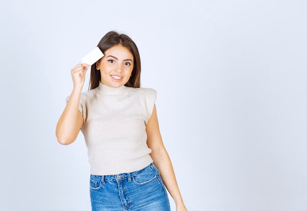 Un modèle de jeune femme souriante tenant une carte et posant sur un mur blanc.