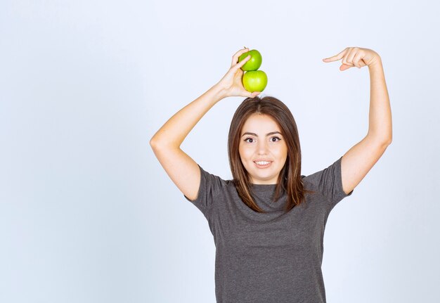 modèle de jeune femme tenant deux pommes vertes au-dessus et les pointant du doigt.