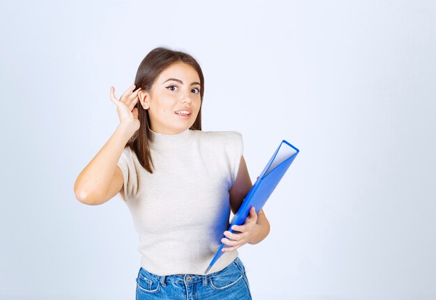 modèle de jeune femme tenant un dossier bleu sur un mur blanc.