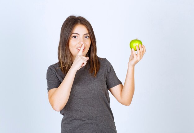 modèle de jeune femme tenant une pomme verte et faisant signe silencieux.