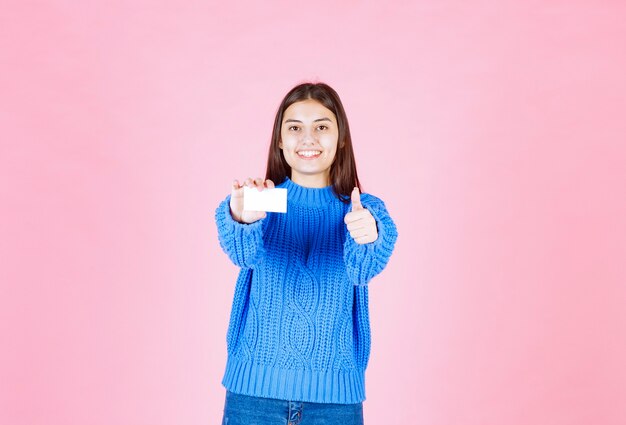 modèle de jeune fille avec une carte montrant un pouce vers le haut sur un mur rose.