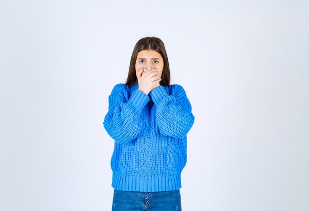 modèle de jeune fille en pull bleu coning bouche avec une main sur blanc-gris.