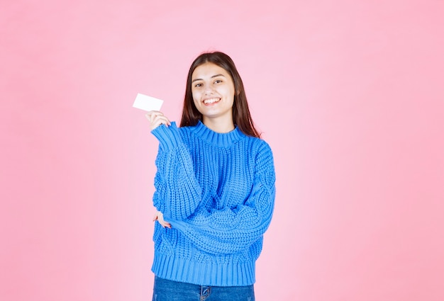 modèle de jeune fille souriante montrant une carte sur le mur rose.