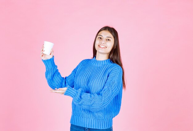 modèle de jeune fille tenant une tasse en plastique sur le mur rose.