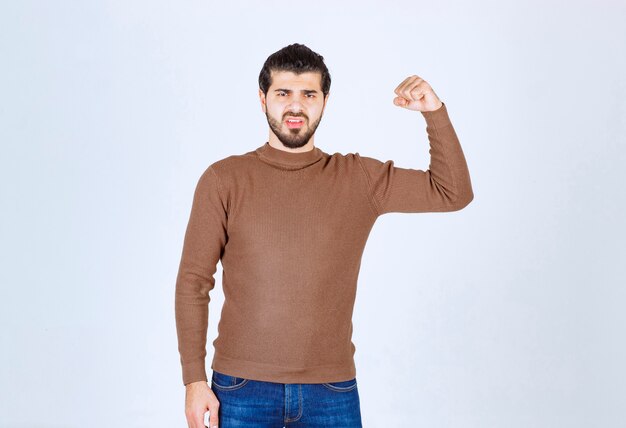 Un modèle de jeune homme gentil debout et montrant ses biceps sur un mur blanc. photo de haute qualité