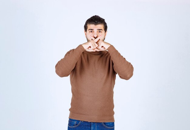 Un modèle de jeune homme séduisant debout et couvrant sa bouche avec les doigts croisés. photo de haute qualité