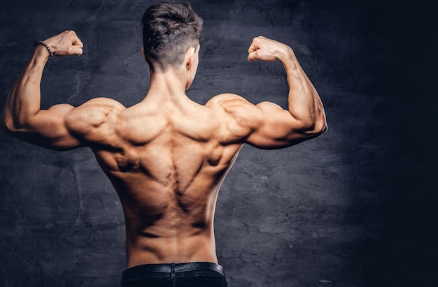 Photo gratuite modèle de jeune homme torse nu fort avec un beau corps montrant ses muscles du dos dans un studio. isolé sur un fond sombre.