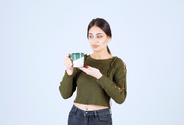 Un modèle de jeune jolie femme tenant une tasse et en détournant les yeux.