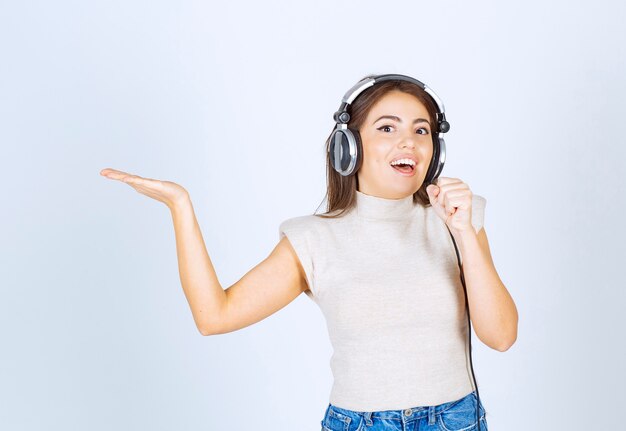 Modèle de jolie femme écoutant de la musique dans les écouteurs et chantant.