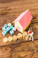 Photo gratuite modèle de maison, clé, blocs de maths et pièces empilées sur toile de fond en bois