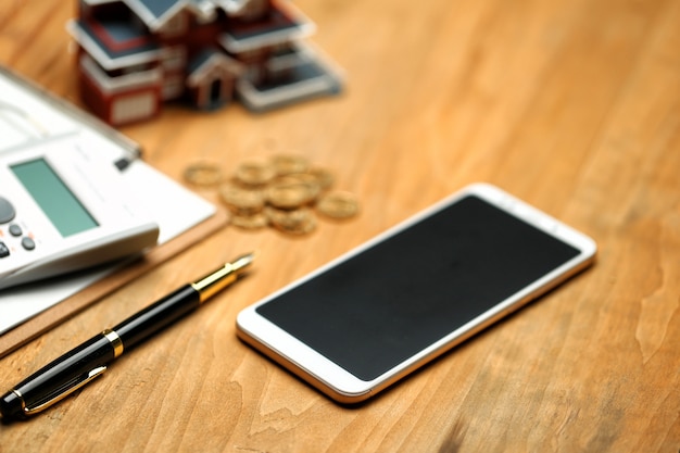 Modèle de maison, smartphone, calculatrice et pièces d'or sur table en bois