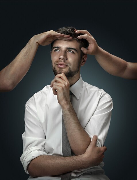 modèle masculin entouré de mains comme ses propres pensées sur fond sombre.