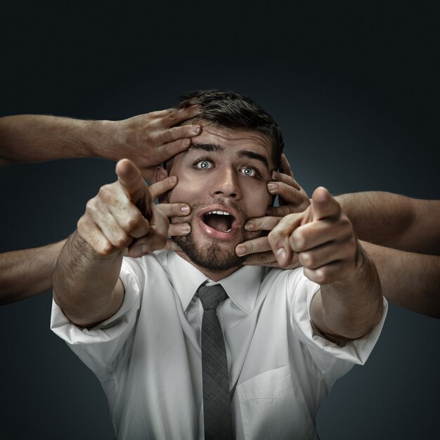 modèle masculin entouré de mains comme ses propres pensées sur fond sombre.