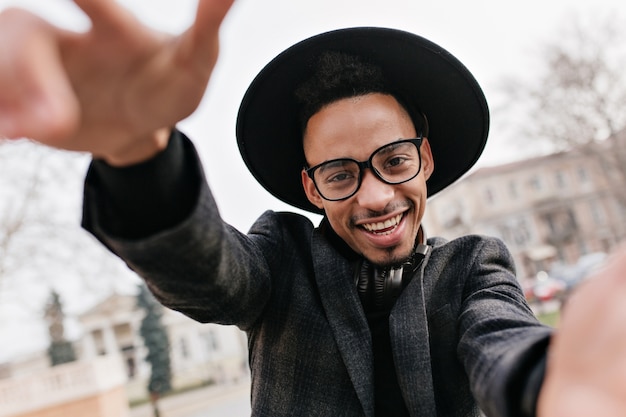 Modèle masculin extatique avec une peau foncée drôle posant sur la ville floue. Superbe homme africain en tenue formelle s'amuser sur le parc.