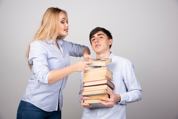 Modèle de mec brune debout et portant une pile de livres près d'une femme blonde