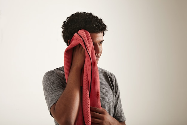 Modèle noir souriant musclé en t-shirt gris en cours d'exécution essuie le côté de son visage avec une serviette rouge à l'écart de