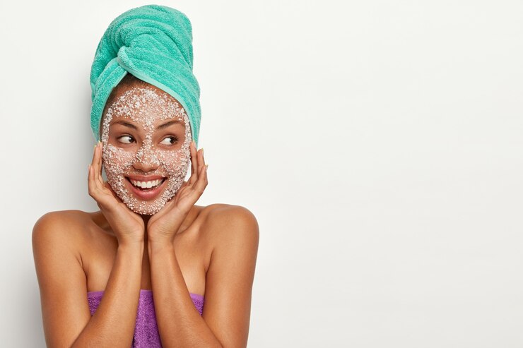 Photo gratuit modèle à peau foncée d'apparence agréable tient les mains sur le visage, applique un masque de gommage, des granules de sel de mer blanc, regarde de côté, est de bonne humeur