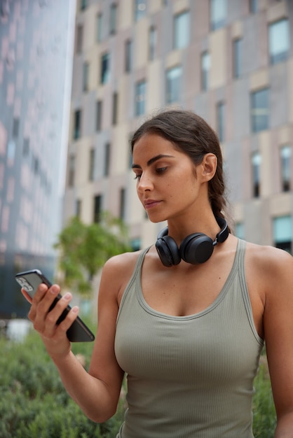 Photo gratuite le modèle a son propre blog de sport tient des montres pour téléphones portables des tutoriels en ligne discutent avec un entraîneur personnel écoute de la musique dans des écouteurs vêtus de poses de vêtements de sport