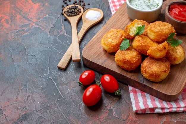 Moitié inférieure vue pépites de poulet sur planche de bois avec sauces tomates cerises cuillères en bois poivre noir sur table sombre espace libre