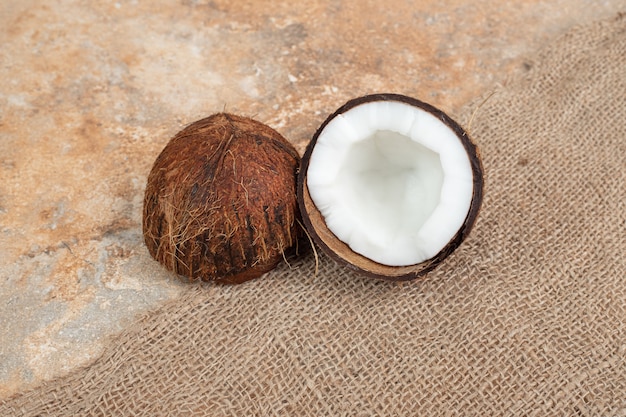 La moitié des noix de coco mûres coupées sur une surface en marbre avec de la toile de jute.