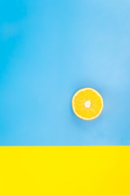 Photo gratuite la moitié d'une orange sur fond bleu et jaune minimalisme à plat