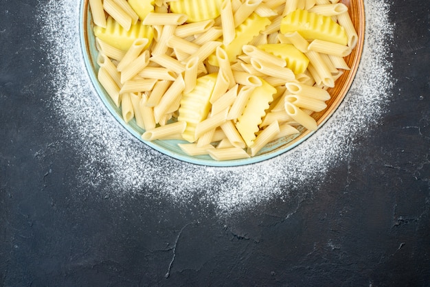 La moitié supérieure des pâtes penne avec pomme de terre dans un bol saupoudré de farine sur noir