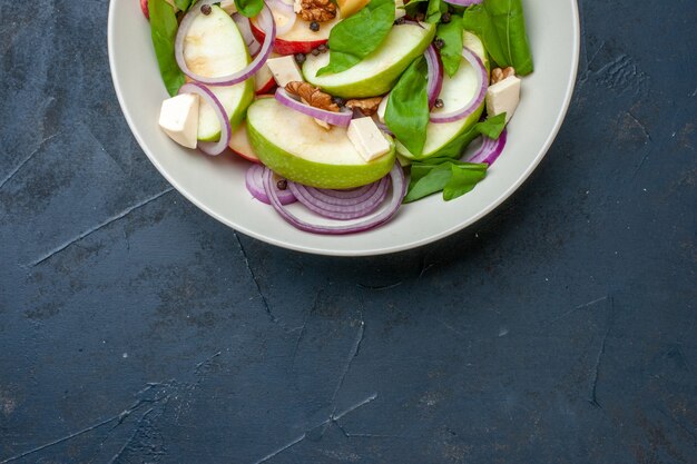 La moitié supérieure de la salade de pommes fraîches dans un bol sur fond bleu foncé