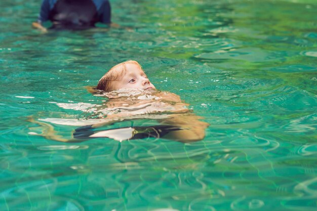 Une monitrice de natation pour enfants enseigne à un garçon heureux à nager dans la piscine