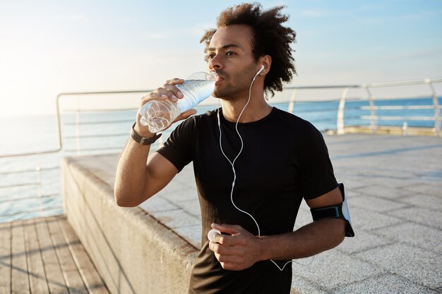 Monter l'eau potable de l'athlète masculin hors de la bouteille en plastique après le jogging sur la poire le matin