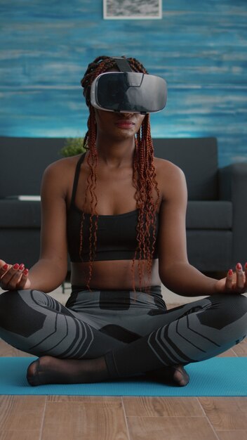 Monter une femme noire portant un casque de réalité virtuelle alors qu'elle était assise sur une carte de yoga