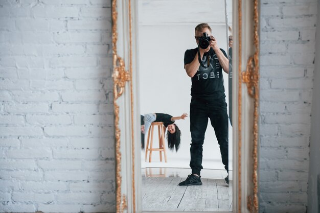 Montrant bonjour. Homme avec appareil photo prenant une photo dans le miroir vintage. Fille s'amuse derrière