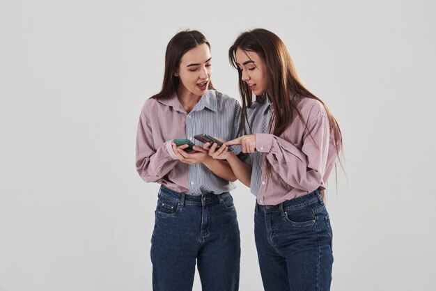 Montre des choses intéressantes dans leurs téléphones. Deux soeurs jumelles debout et posant