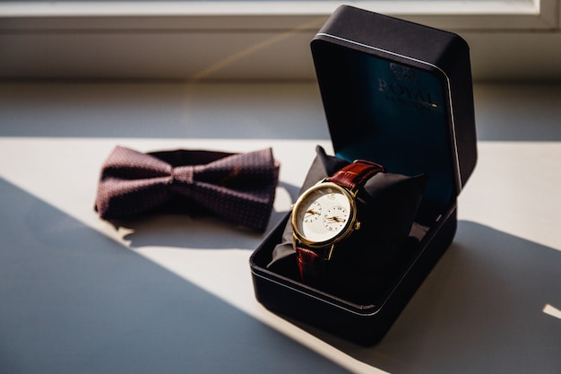 Montre dans une boîte noire et un nœud papillon sur le rebord de la fenêtre blanche