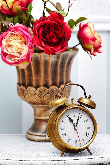 Photo gratuite montre horloge classique dans un intérieur rétro coloré lumineux derrière des fleurs rouges