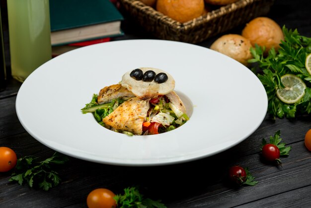 Un morceau de filet de poisson grillé avec une salade verte et des baies dans une assiette blanche.