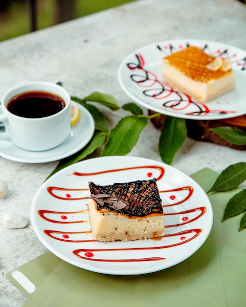 Morceau de gâteau au fromage garni de sirop de chocolat servi avec du thé