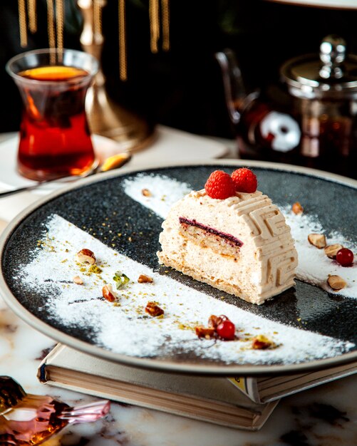 Morceau de gâteau décoré de framboises et verre de thé sur la table