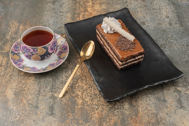 Un morceau de gâteau avec du thé chaud et une cuillère sur une assiette sombre