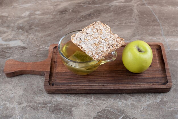 Un morceau de gâteau de riz soufflé, thé et pomme, sur le plateau en bois, sur la surface en marbre