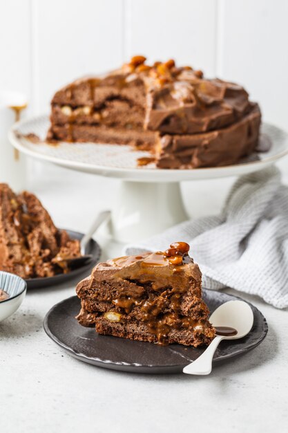 Morceau De Gateau De Snickers Fait Maison Avec Creme Au Chocolat Et Caramel Sur Une Soucoupe Noire Fond Blanc Photo Premium