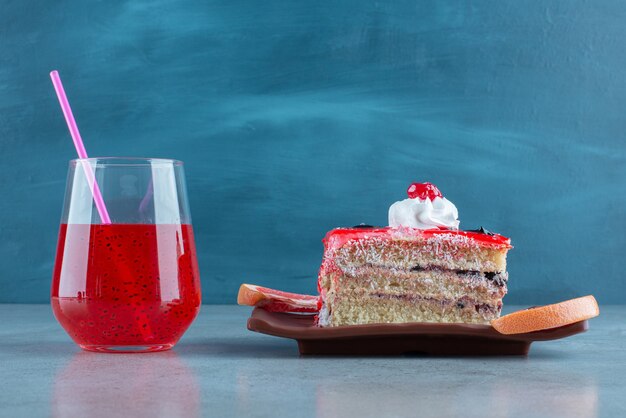 Un morceau de gâteau avec une tasse en verre de jus rouge.
