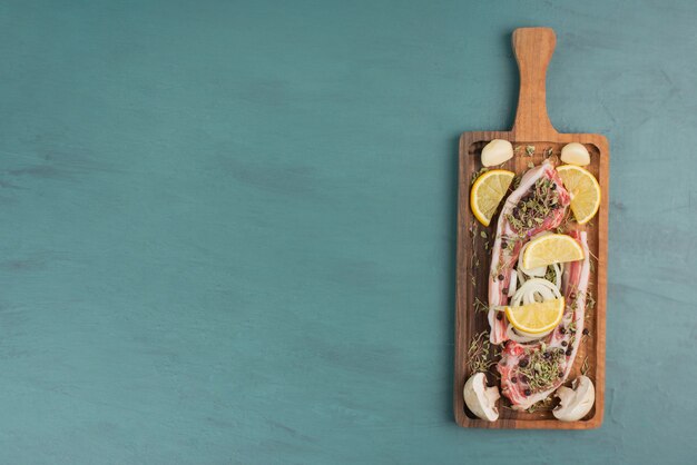 Morceau de viande non cuit avec des légumes sur table bleue.