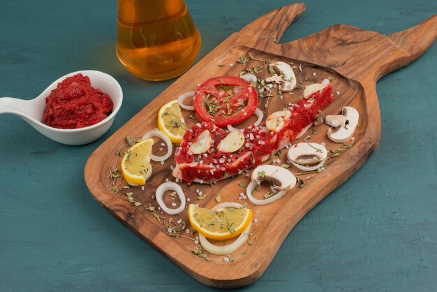 Morceau de viande non cuit avec des légumes sur table bleue.