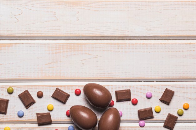 Morceaux de chocolat; oeufs de pâques et bonbons aux pierres précieuses au bas du bureau en bois