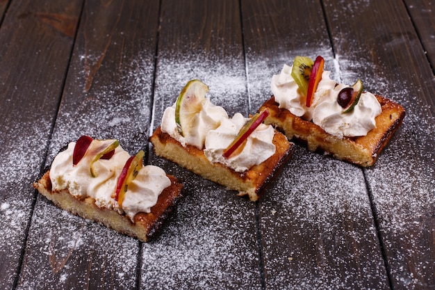 Photo gratuite morceaux de gâteau avec des fruits couverts de sucre en poudre servi sur une table en bois