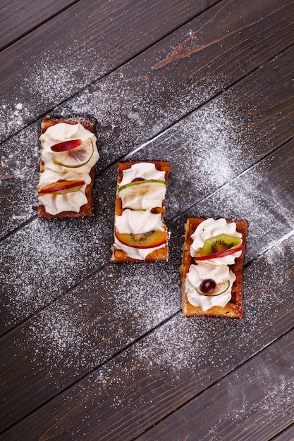 Morceaux de gâteau avec des fruits couverts de sucre en poudre servi sur une table en bois